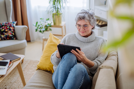 Woman in cosy living room relaxing with e-reader on couch
