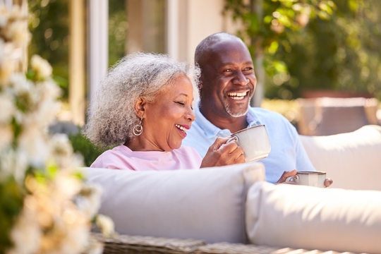 smiling senior couple drinking coffee on outdoor couch