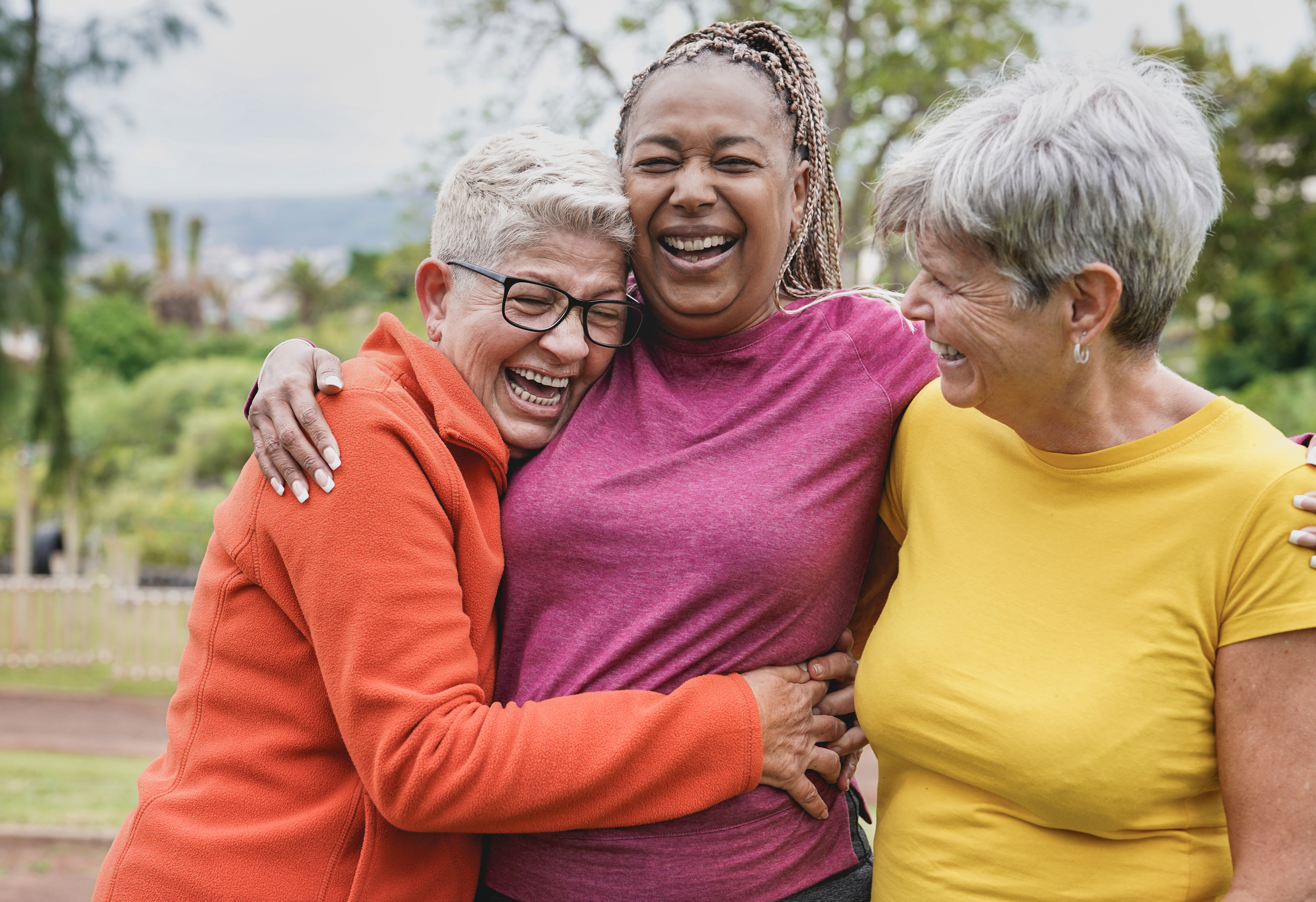 three active senior friends laughing and hugging outdoors