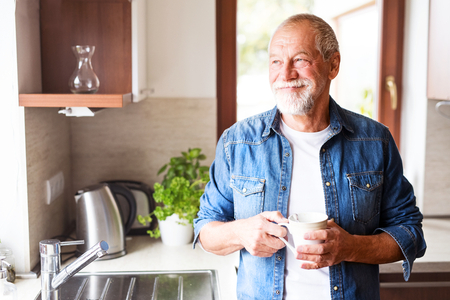 smiling senior man with coffee cup in kitchen