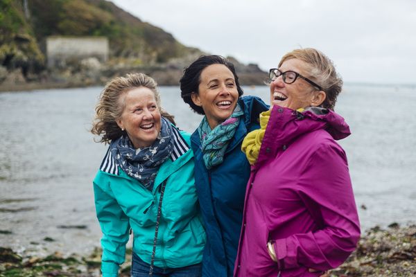 three women laughing on windy day on rocky shore