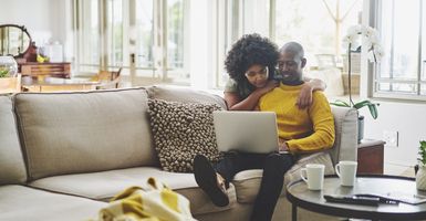 young man and woman sitting on couch working on laptop