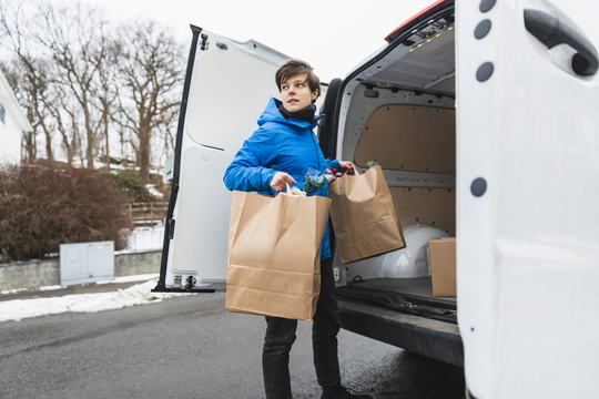 woman unloading paper bagged groceries from delivery truck